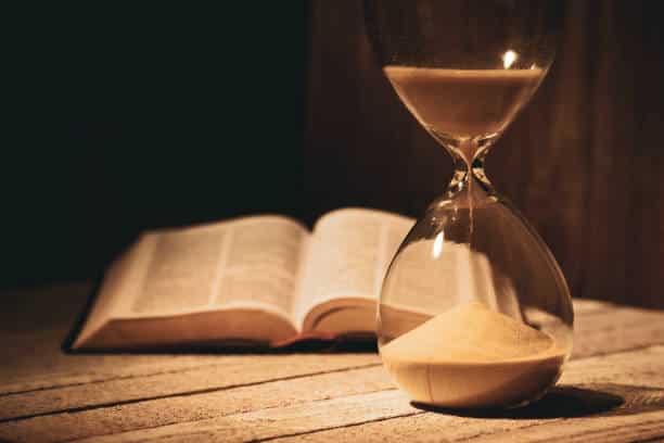 An open bible with an hourglass in front of it